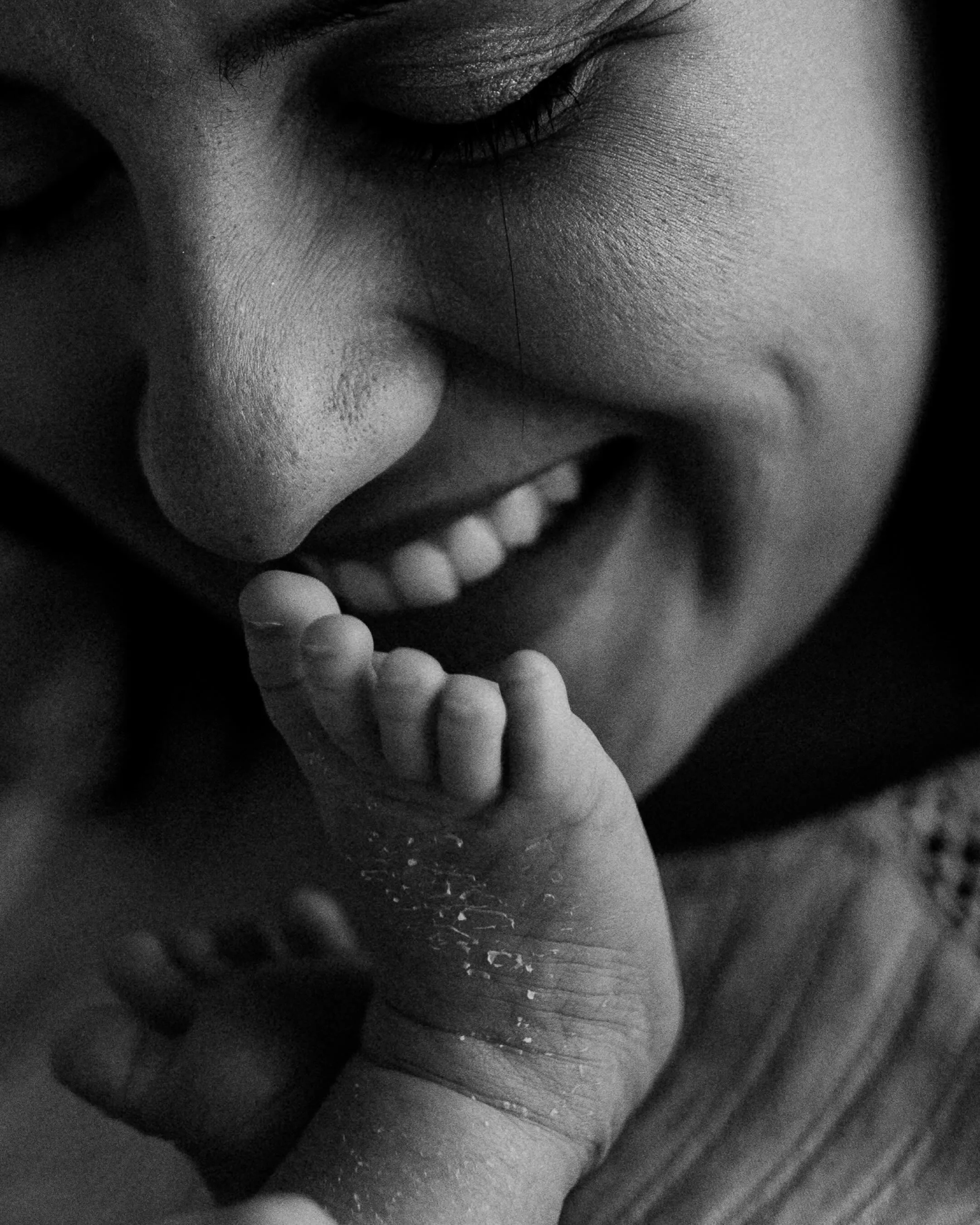 Detalhe em preto e branco de um sorriso e da pequena mão de um bebê sobre o rosto