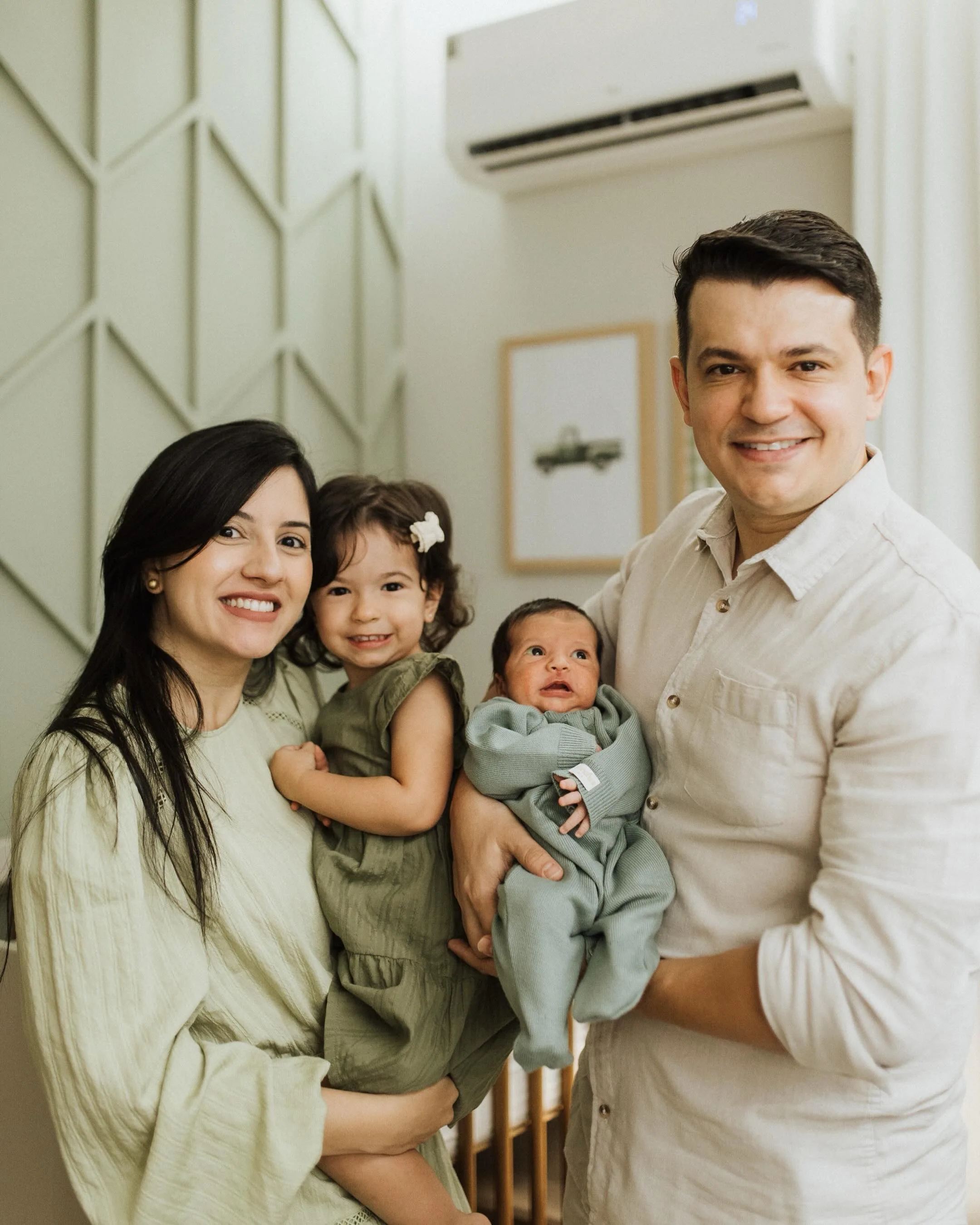 Dois adultos posam juntos com uma criança e um bebê em um quarto