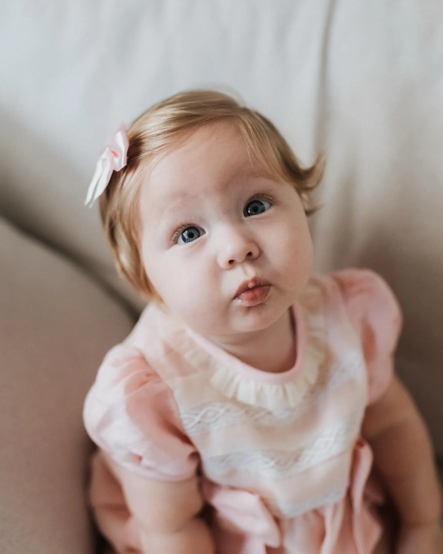 Bebê de vestido rosa claro olha para a câmera em um sofá